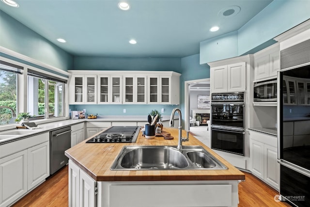 kitchen with black appliances, white cabinetry, sink, and a kitchen island with sink