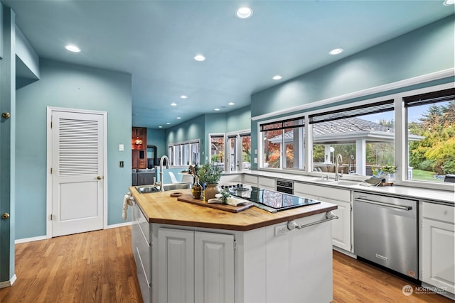 kitchen featuring butcher block countertops, a center island with sink, light hardwood / wood-style floors, white cabinets, and stainless steel dishwasher