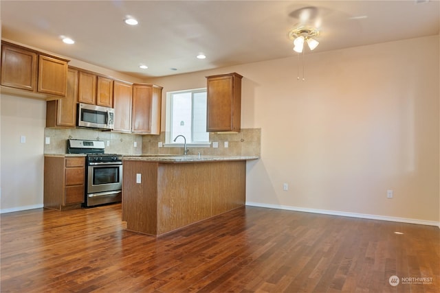 kitchen featuring appliances with stainless steel finishes, decorative backsplash, light stone counters, kitchen peninsula, and dark wood-type flooring