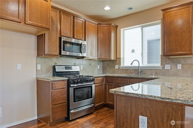 kitchen with sink, dark wood-type flooring, appliances with stainless steel finishes, backsplash, and light stone counters