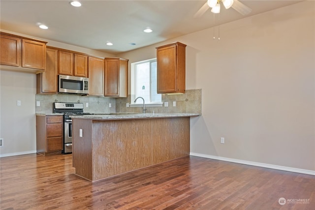 kitchen with light stone counters, appliances with stainless steel finishes, dark hardwood / wood-style flooring, kitchen peninsula, and decorative backsplash