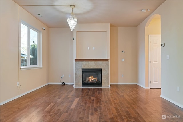 unfurnished living room with hardwood / wood-style flooring, a tile fireplace, and a chandelier