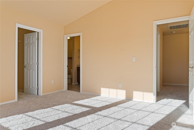 unfurnished bedroom featuring ensuite bath, lofted ceiling, light colored carpet, and a walk in closet