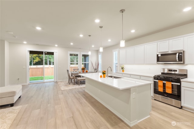 kitchen featuring light hardwood / wood-style floors, a center island with sink, sink, appliances with stainless steel finishes, and hanging light fixtures