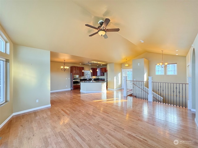 unfurnished living room with vaulted ceiling, ceiling fan with notable chandelier, and light hardwood / wood-style flooring