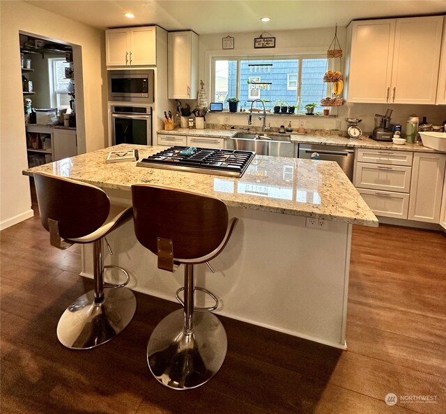 kitchen featuring stainless steel appliances, a kitchen island, sink, white cabinets, and dark wood-type flooring