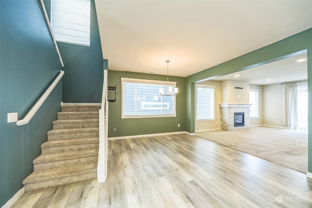 unfurnished living room with a fireplace, an inviting chandelier, and light hardwood / wood-style flooring