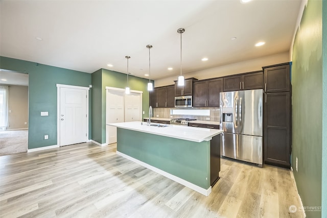 kitchen featuring stainless steel appliances, dark brown cabinetry, a kitchen island with sink, pendant lighting, and light hardwood / wood-style flooring