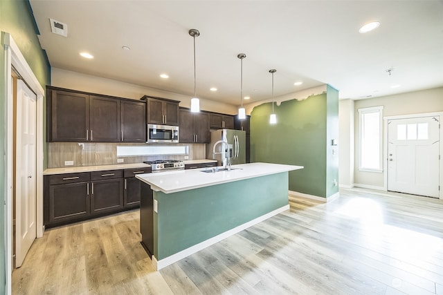 kitchen featuring light hardwood / wood-style floors, dark brown cabinets, a center island with sink, and stainless steel appliances