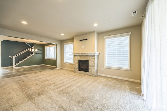 unfurnished living room with light colored carpet, a chandelier, and a tiled fireplace