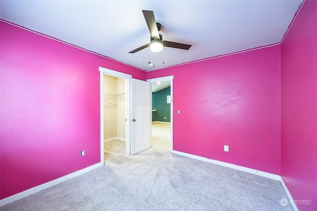 unfurnished bedroom with ceiling fan, light carpet, a closet, and a walk in closet