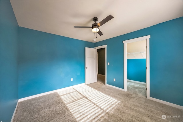 unfurnished bedroom with ceiling fan, a closet, a walk in closet, and light colored carpet