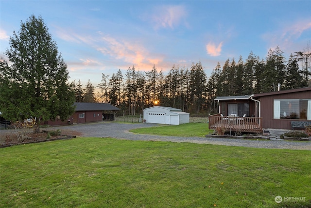 yard at dusk featuring a garage, an outbuilding, and a deck