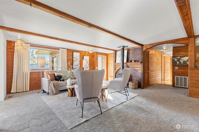 carpeted dining room with a wood stove, wooden walls, and beamed ceiling