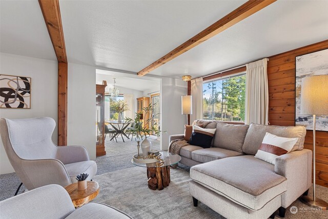 carpeted living room with beamed ceiling, a notable chandelier, and wooden walls