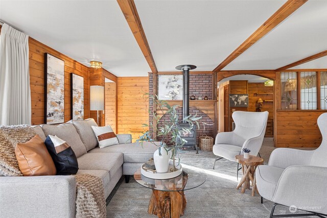 carpeted living room with wood walls, a wood stove, beam ceiling, and ornamental molding