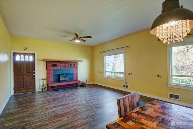 unfurnished living room with a fireplace, plenty of natural light, dark wood-type flooring, and ceiling fan with notable chandelier