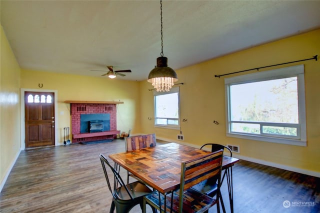 dining space featuring a fireplace, ceiling fan with notable chandelier, dark wood-type flooring, and a healthy amount of sunlight