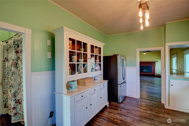 kitchen with dark hardwood / wood-style flooring, a brick fireplace, ornamental molding, white cabinets, and stainless steel refrigerator