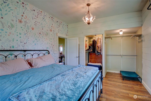 bedroom featuring a spacious closet, an inviting chandelier, wood walls, light hardwood / wood-style floors, and a closet