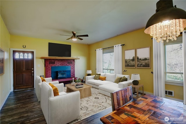 living room featuring a fireplace, ceiling fan with notable chandelier, and dark wood-type flooring