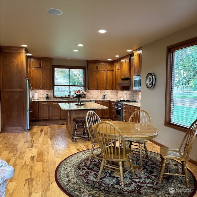 kitchen with sink, light hardwood / wood-style flooring, light stone countertops, a kitchen island, and stainless steel appliances