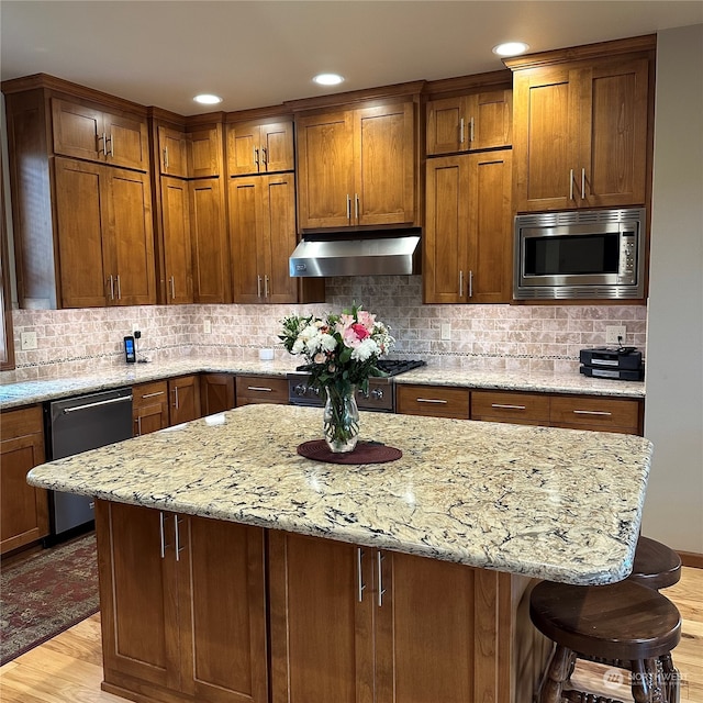 kitchen with a kitchen breakfast bar, light wood-type flooring, backsplash, light stone counters, and stainless steel appliances