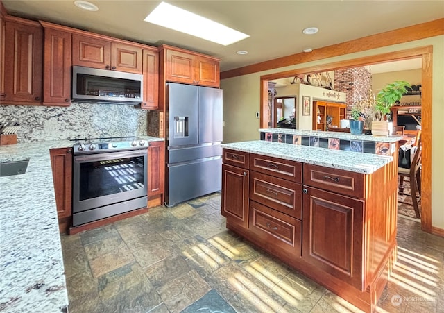 kitchen with light stone countertops, stainless steel appliances, tasteful backsplash, a breakfast bar area, and a kitchen island