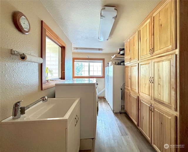 laundry room with washer and clothes dryer, cabinets, a textured ceiling, and light hardwood / wood-style flooring