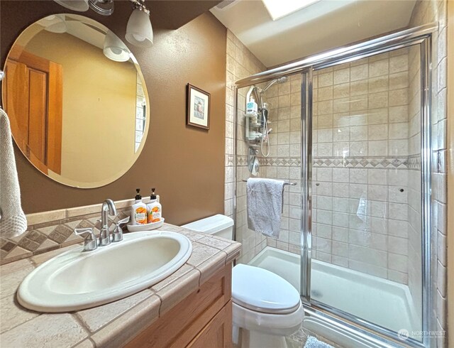 bathroom featuring a shower with door, vanity, and toilet