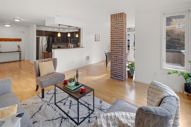 living room with sink, light wood-type flooring, track lighting, and ornate columns