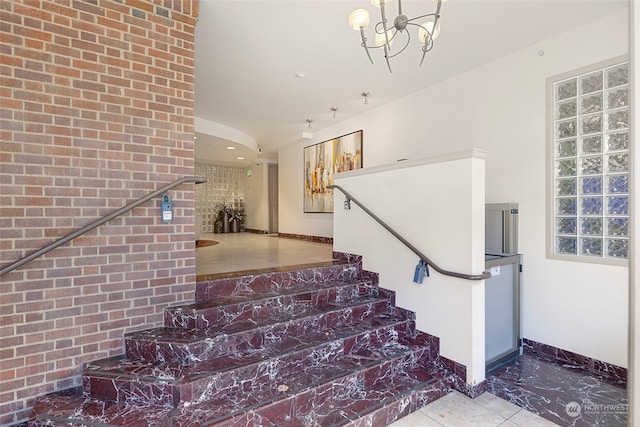 stairs featuring brick wall, tile patterned floors, and an inviting chandelier