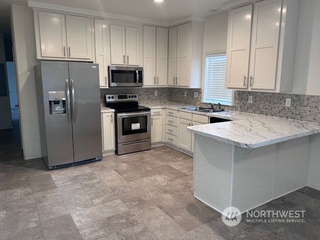 kitchen featuring kitchen peninsula, sink, backsplash, white cabinetry, and appliances with stainless steel finishes