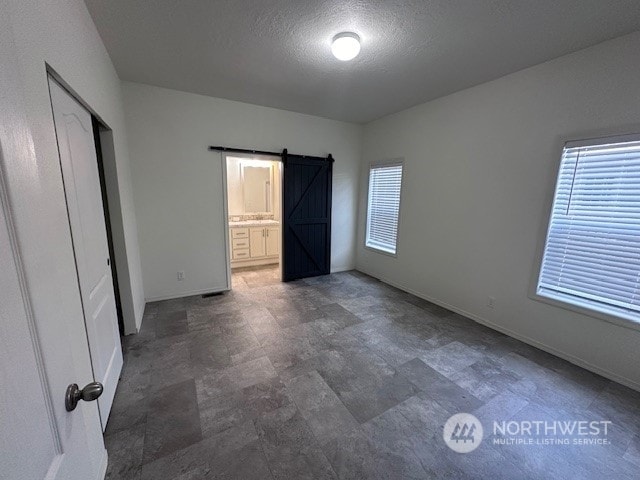 unfurnished bedroom featuring a textured ceiling, a closet, a barn door, and ensuite bathroom