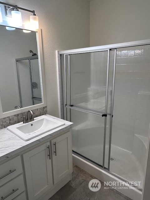 bathroom featuring a shower with door, vanity, and decorative backsplash