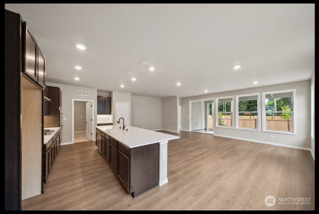 kitchen with light wood-type flooring, dark brown cabinetry, sink, and an island with sink