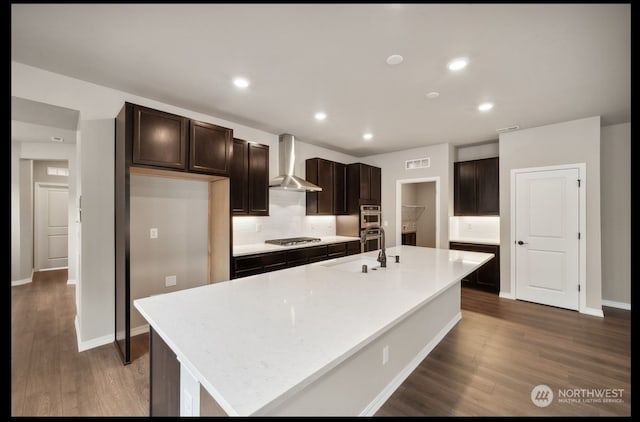 kitchen with an island with sink, wall chimney exhaust hood, sink, and appliances with stainless steel finishes