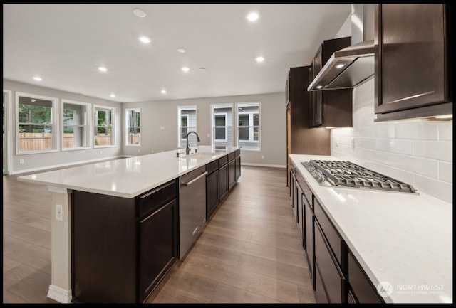 kitchen featuring stainless steel appliances, a center island with sink, sink, light hardwood / wood-style flooring, and wall chimney range hood