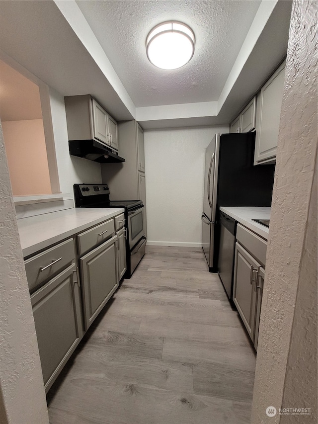 kitchen with appliances with stainless steel finishes, a textured ceiling, gray cabinets, and light hardwood / wood-style flooring