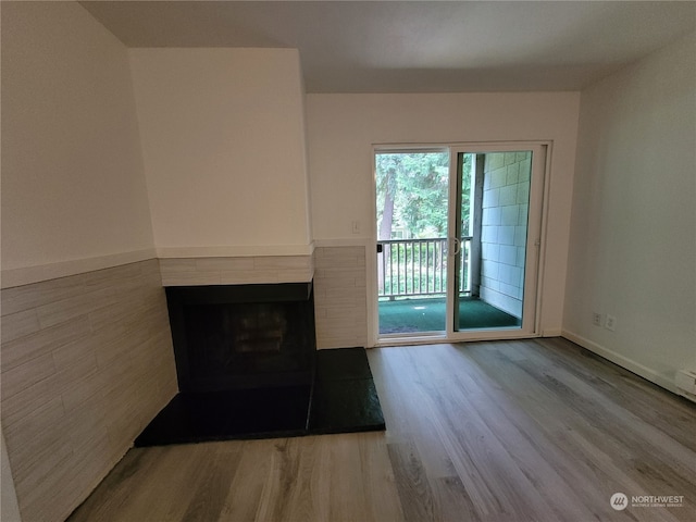 unfurnished living room with a tiled fireplace and wood-type flooring