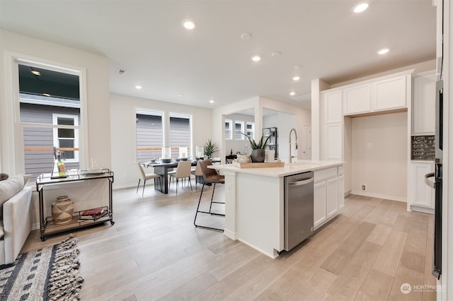 kitchen featuring stainless steel dishwasher, a kitchen island with sink, sink, light hardwood / wood-style flooring, and white cabinetry