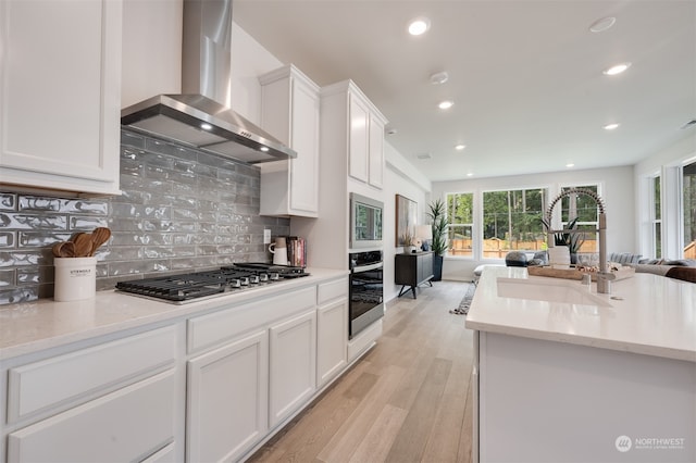 kitchen with sink, stainless steel appliances, wall chimney range hood, light hardwood / wood-style flooring, and white cabinets