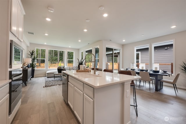 kitchen featuring sink, an island with sink, appliances with stainless steel finishes, light hardwood / wood-style floors, and white cabinetry