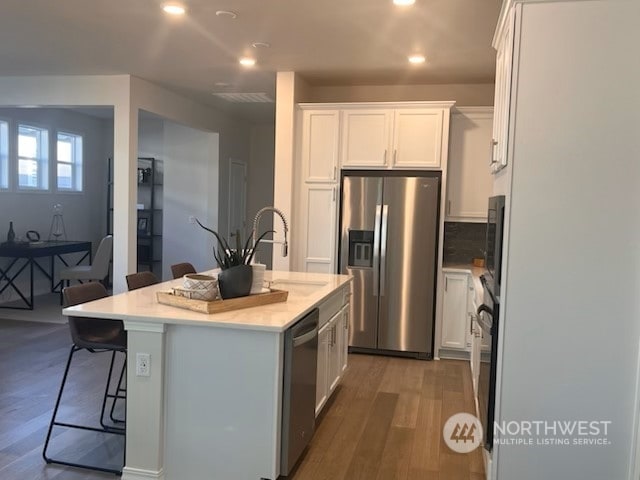 kitchen with a center island with sink, white cabinets, stainless steel appliances, and hardwood / wood-style flooring