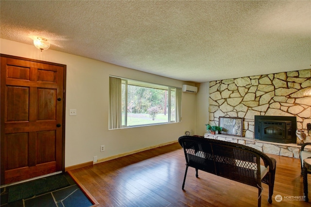 interior space featuring a stone fireplace, wood-type flooring, a wall mounted air conditioner, and a textured ceiling