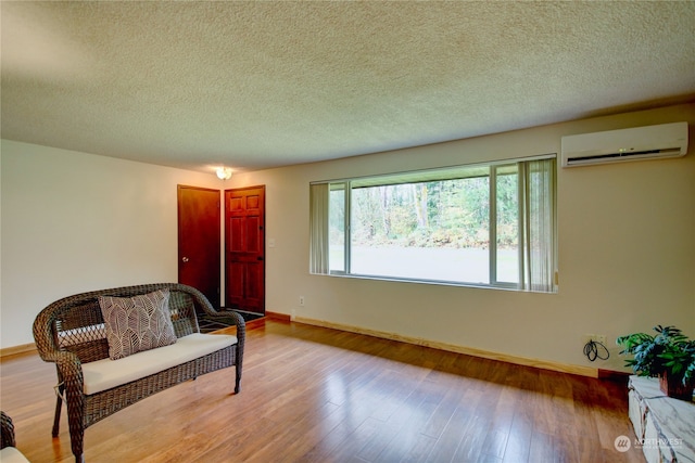 sitting room featuring a textured ceiling, light wood-type flooring, and a wall mounted air conditioner