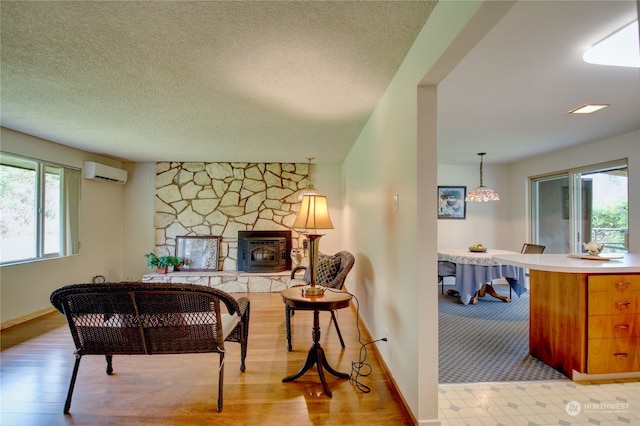 sitting room with a wealth of natural light, light hardwood / wood-style floors, an AC wall unit, and a wood stove