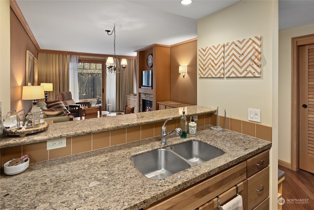 kitchen with a notable chandelier, sink, dark hardwood / wood-style floors, light stone countertops, and decorative light fixtures