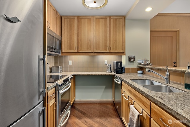 kitchen with tasteful backsplash, appliances with stainless steel finishes, light stone countertops, sink, and hardwood / wood-style floors