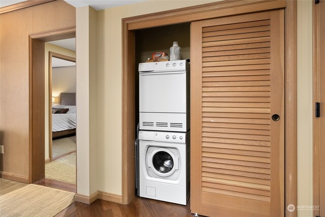 clothes washing area featuring stacked washer and dryer and dark wood-type flooring